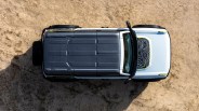 Top-down view of a white and black off-road vehicle with a patterned hood, parked on sandy ground.