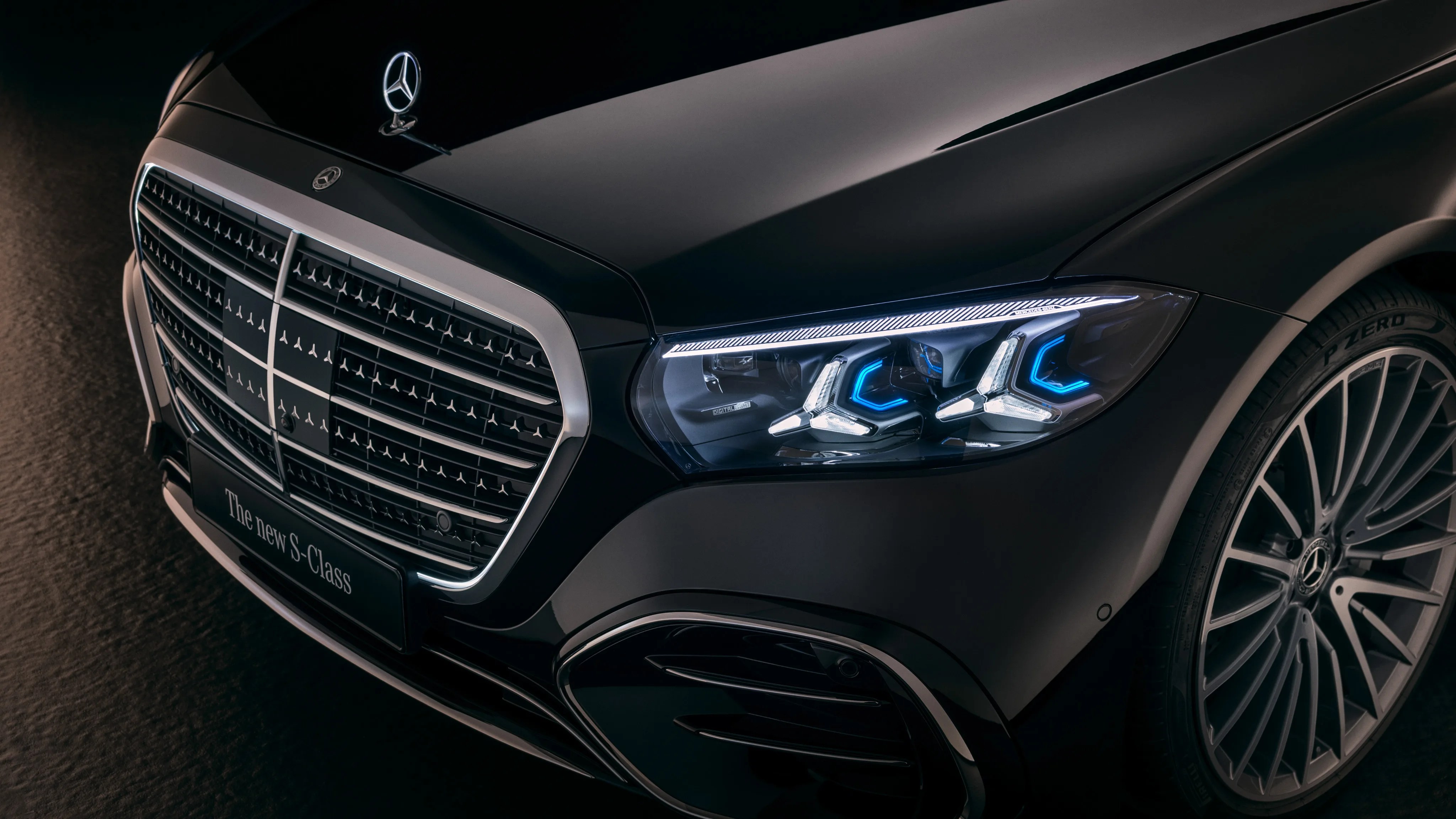 Front view of a black Mercedes-Benz S-Class showing the grille, illuminated headlight, and alloy wheel.