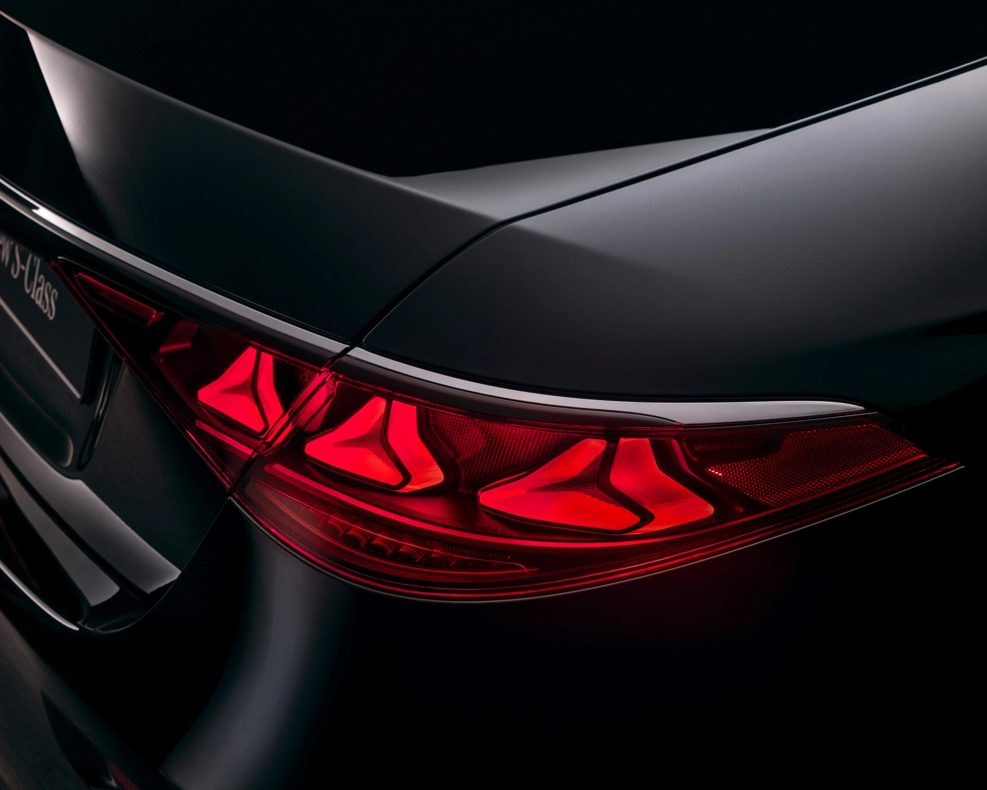 Close-up of a sleek black car's rear with illuminated red taillights and a subtle chrome trim.