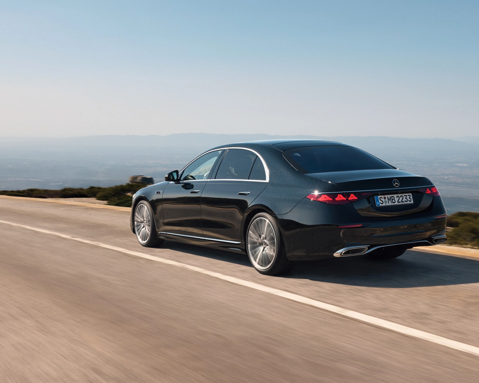 Black Mercedes-Benz luxury sedan driving on a mountain road with clear sky in the background.