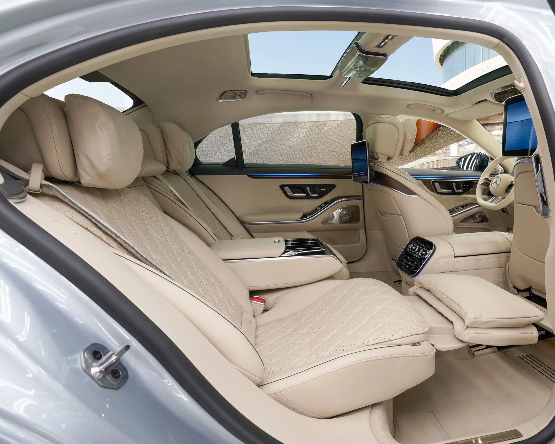 Beige leather luxury car interior with quilted seats, rear entertainment screens, and panoramic sunroof.