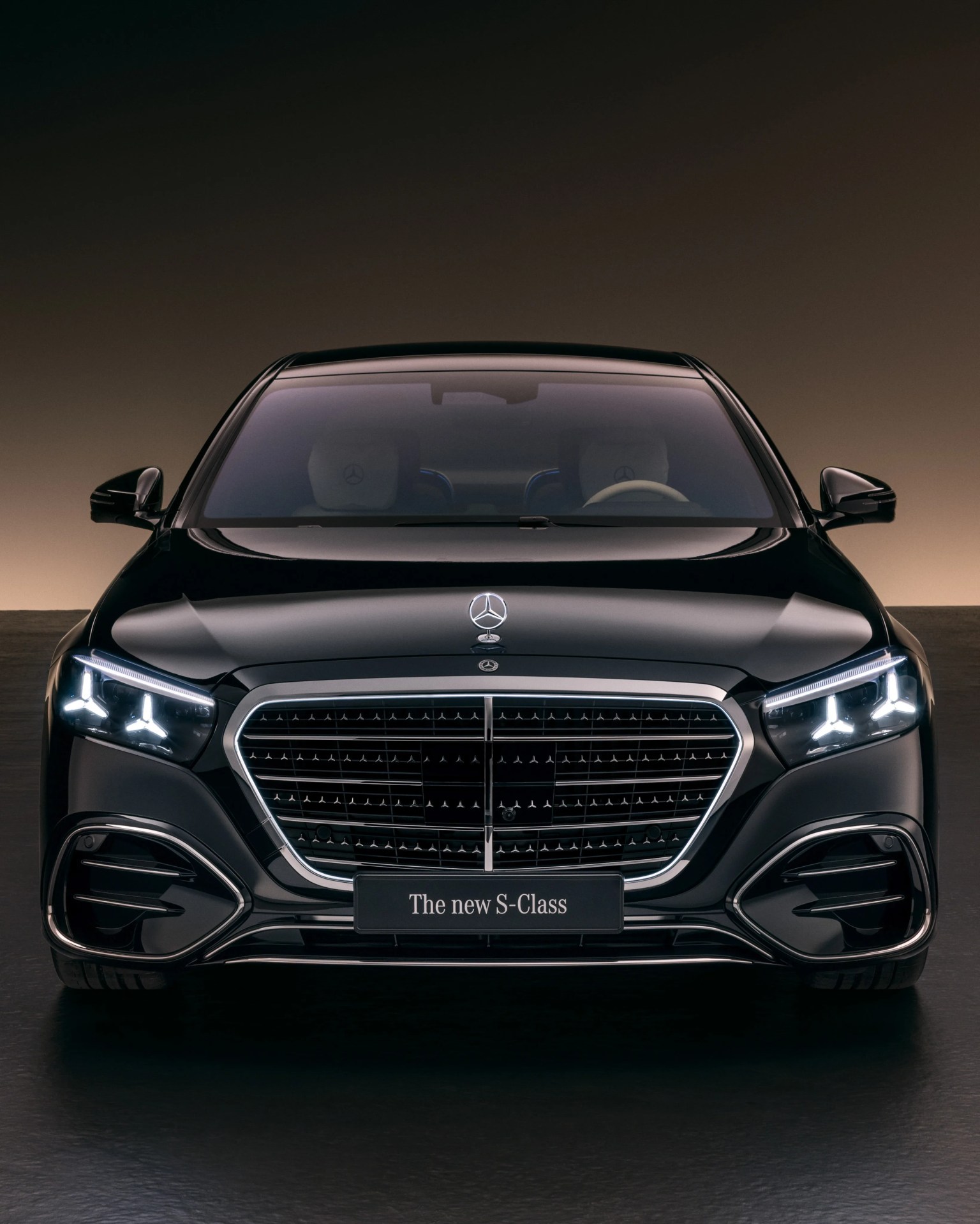 Front view of a black Mercedes-Benz S-Class sedan with illuminated headlights and a prominent grille.