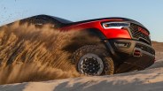 Red and black RAM truck kicking up sand while driving off-road on a sandy terrain.
