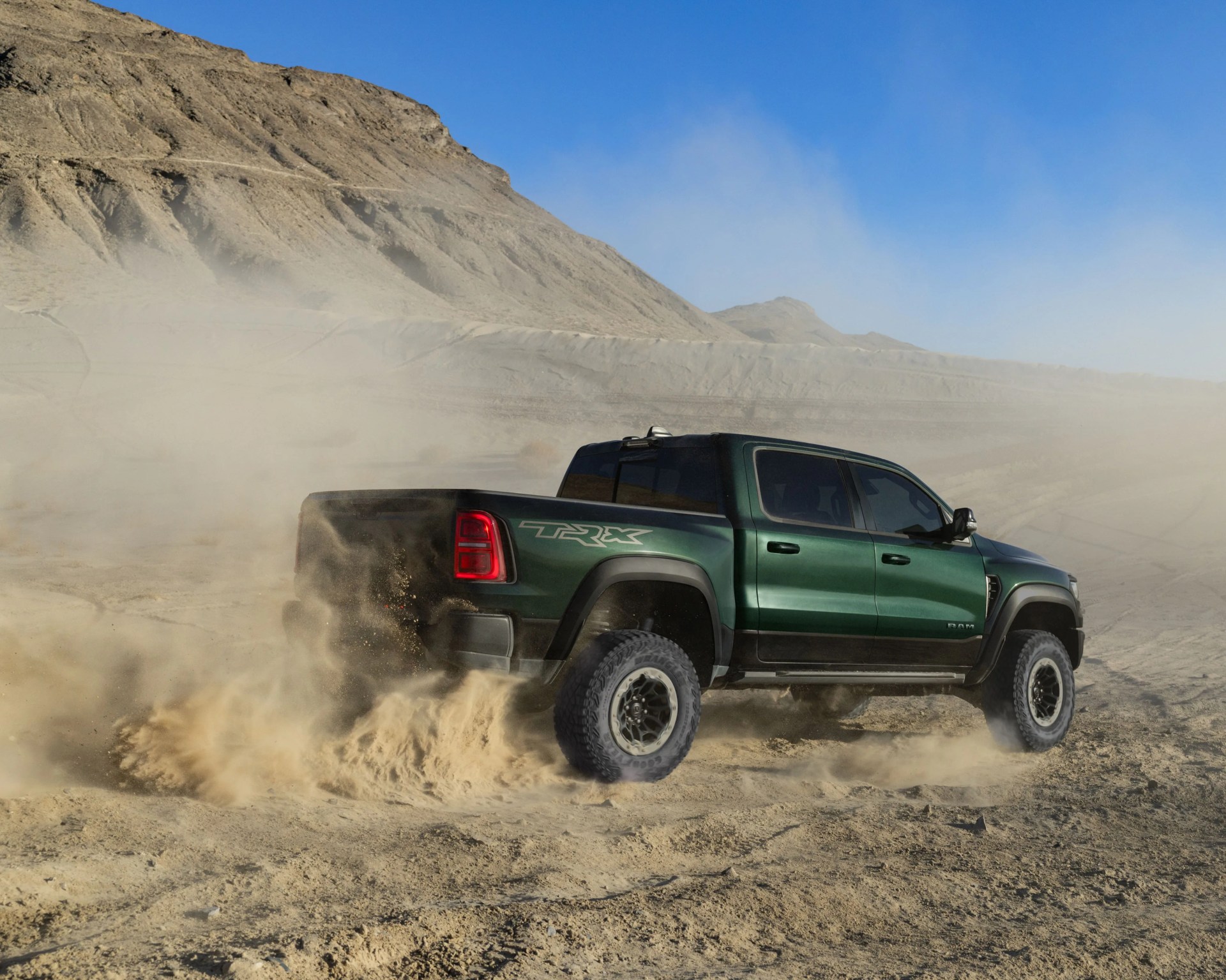 Green Ram TRX pickup truck kicking up dust while driving on a dry, rocky desert terrain.
