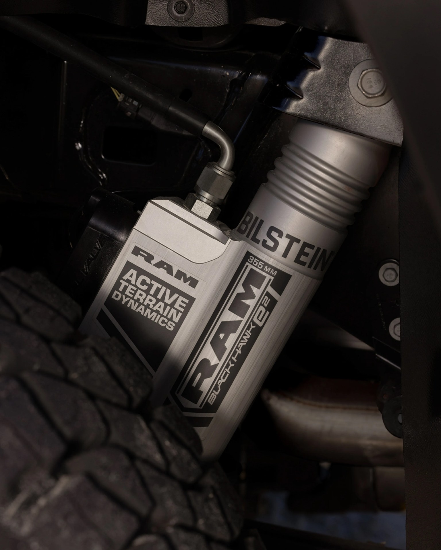 Silver RAM Active Terrain Dynamics shock absorber with Bilstein branding near a black off-road tire.