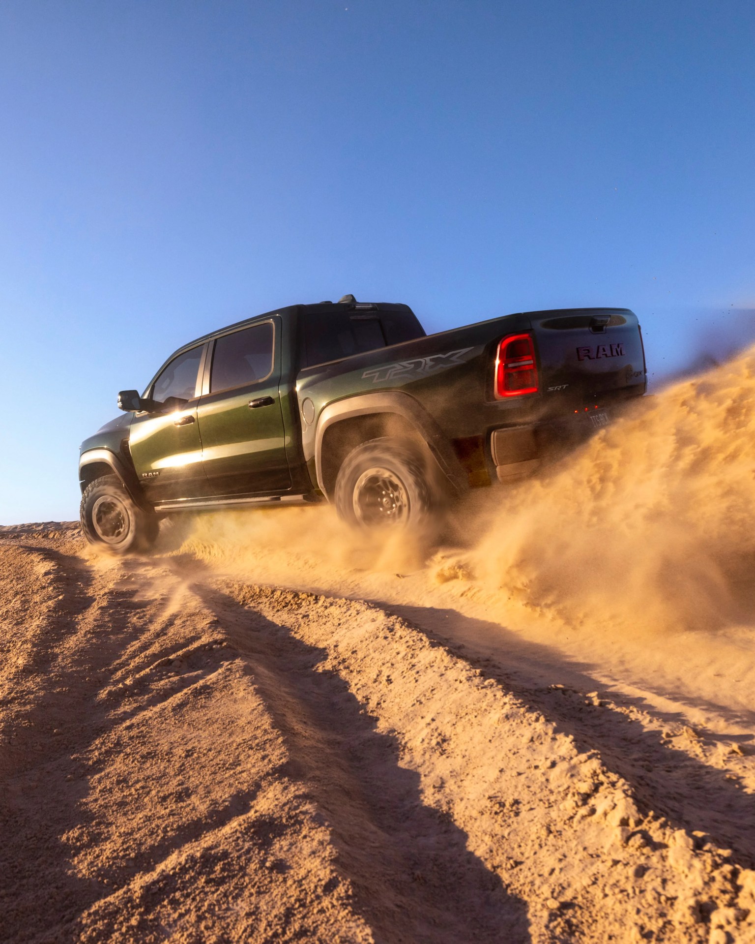 Green RAM TRX pickup truck kicking up dust while driving off-road on a dirt trail under clear blue sky.