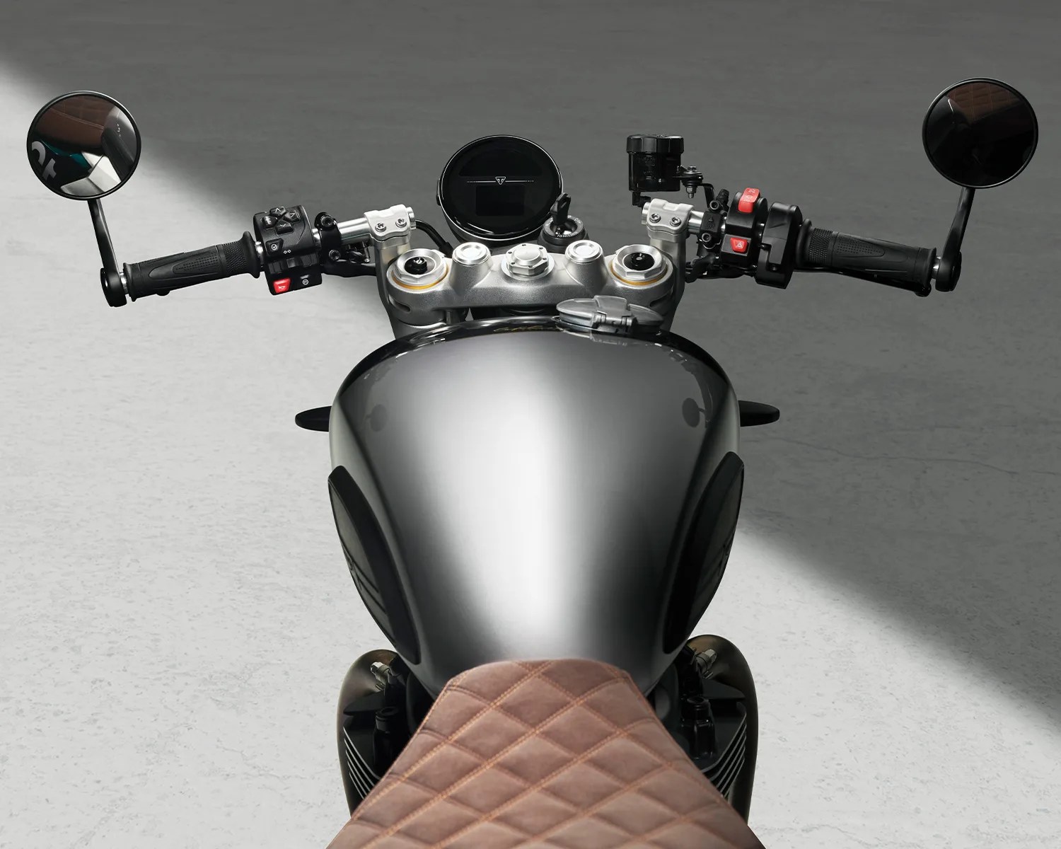 Glossy metallic gray motorcycle fuel tank with brown diamond-stitched seat and black handlebars with round mirrors.