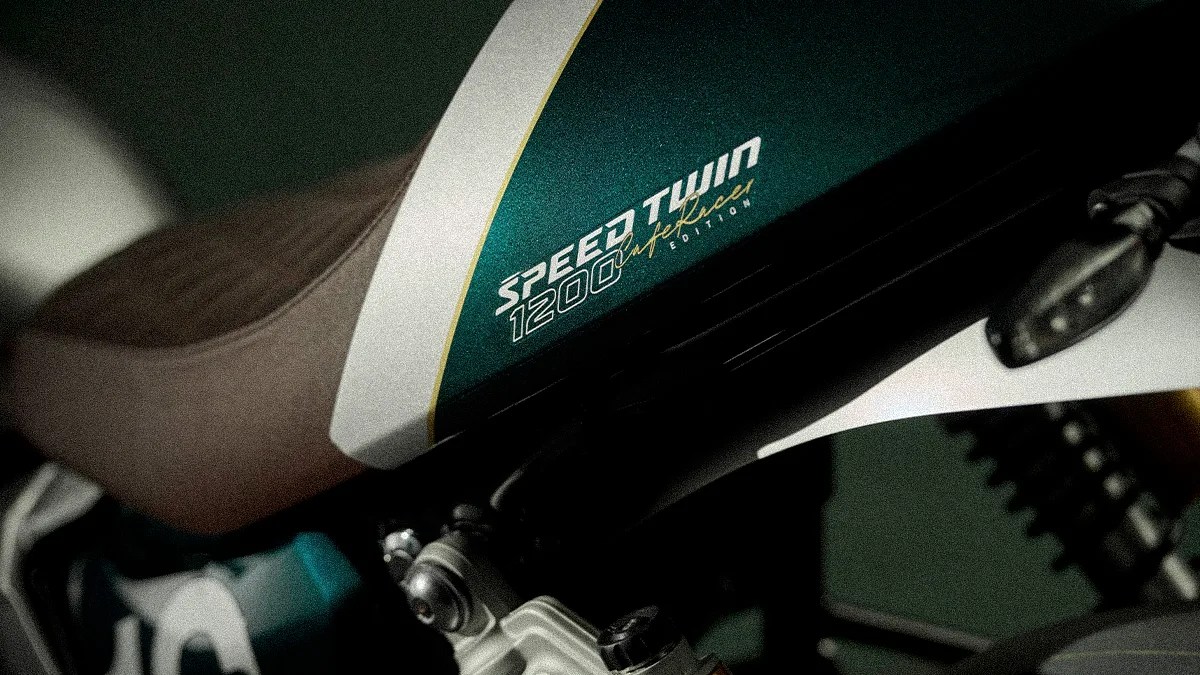 Close-up of a green and white motorcycle fuel tank with "Speed Twin 1200" and "CAFÉ RACER EDITION" text near a brown seat.