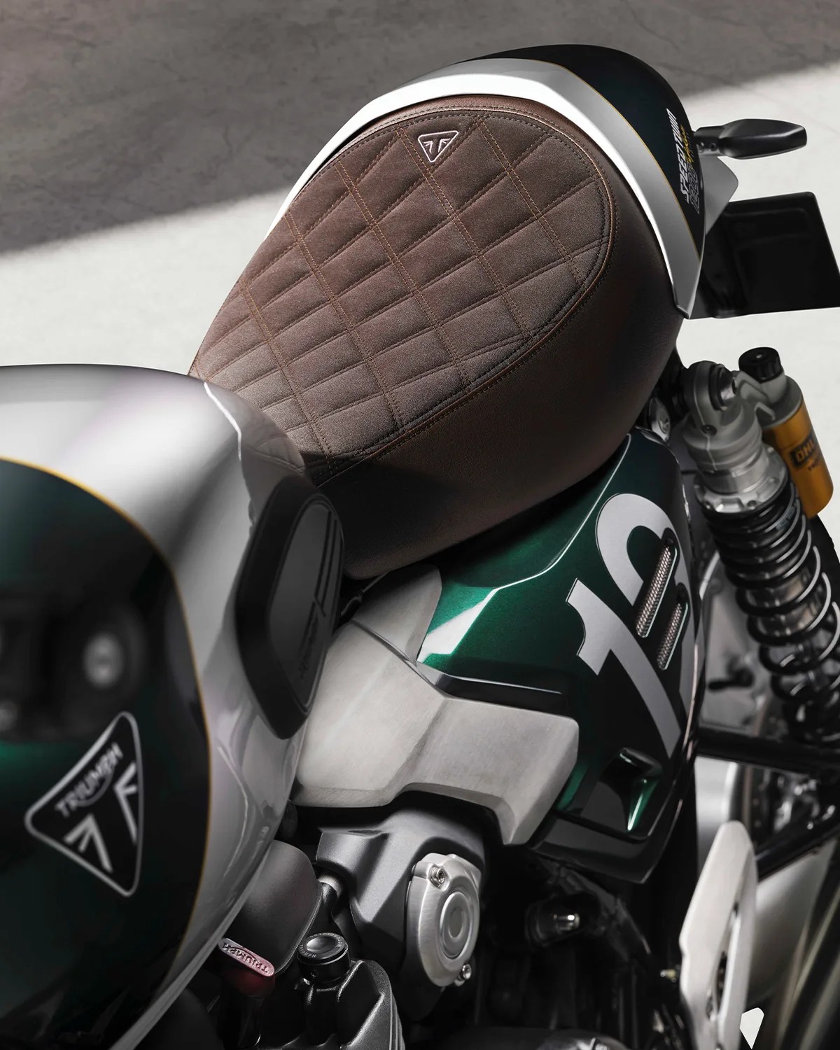 Brown quilted leather seat on a green and silver Triumph motorcycle with visible suspension and fuel tank.