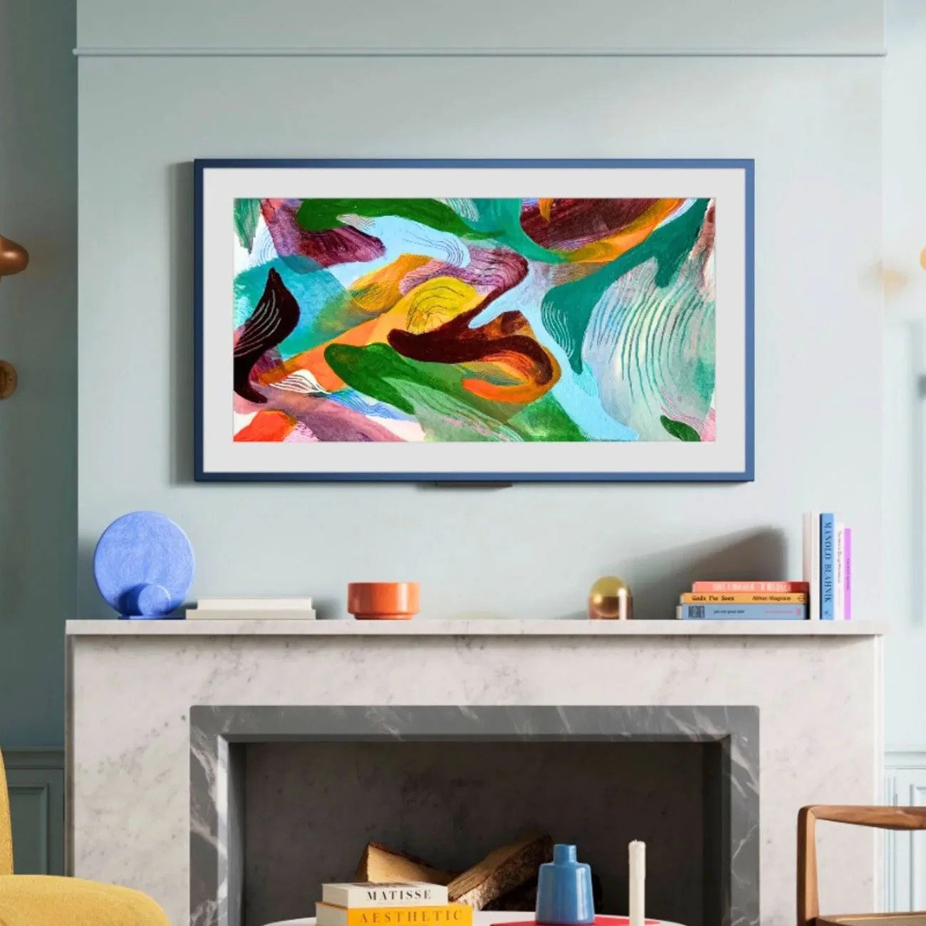 Abstract colorful painting with green, orange, blue, and purple brushstrokes in a blue frame above a marble fireplace.