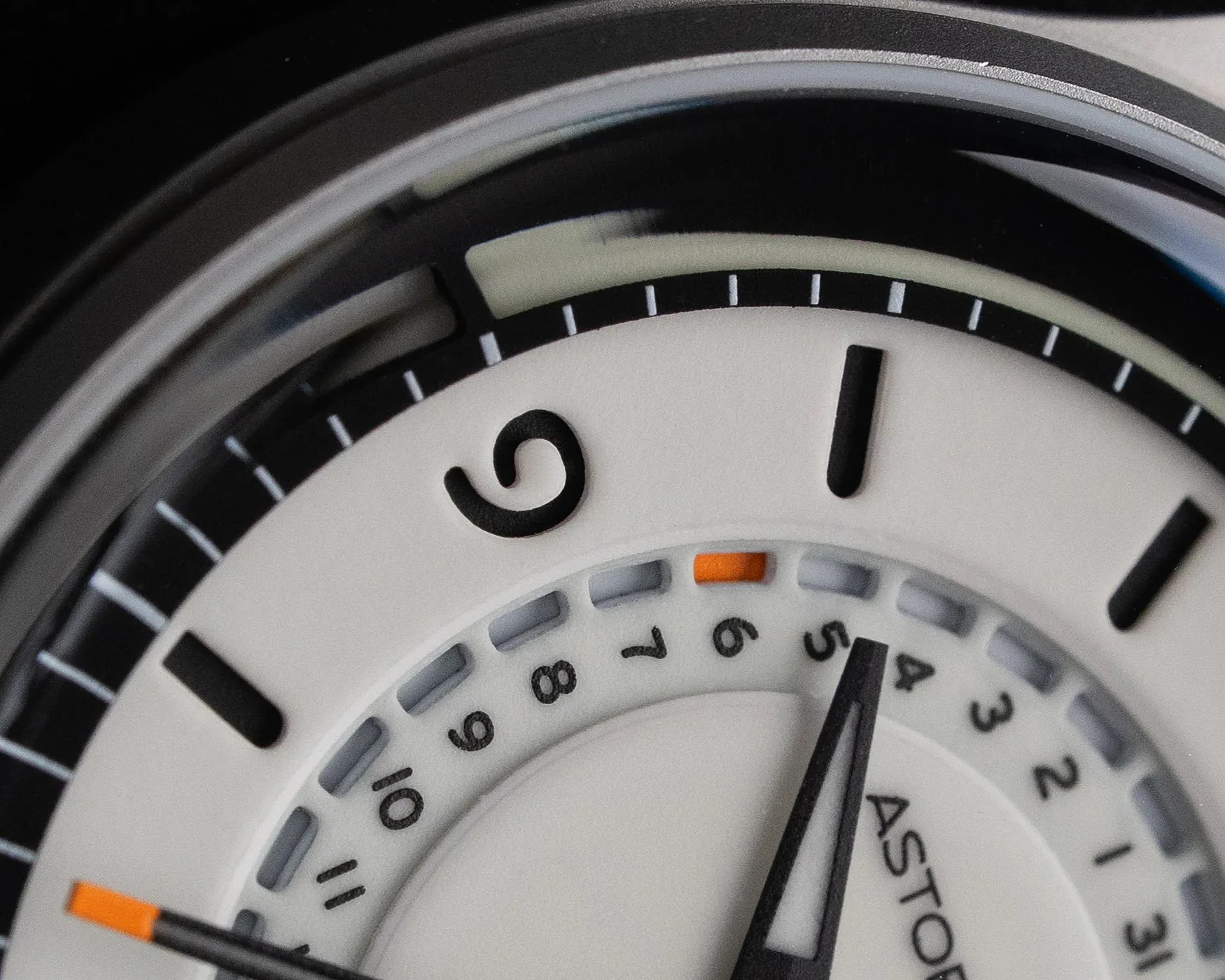 Close-up of a white watch dial with black hour markers, an orange date indicator, and black hands.