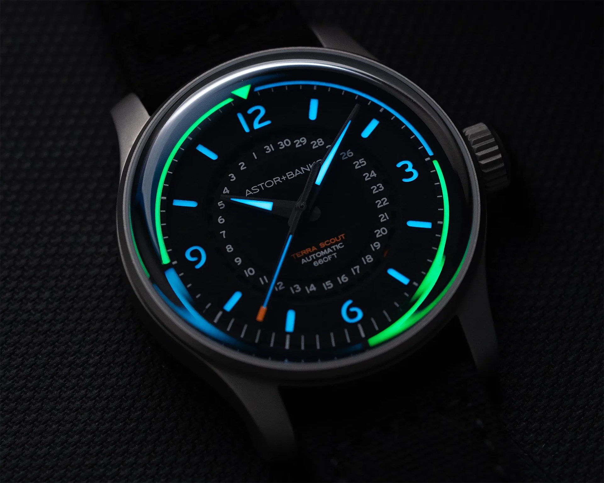 Black wristwatch with blue and green luminescent hour markers and hands on a dark textured surface.