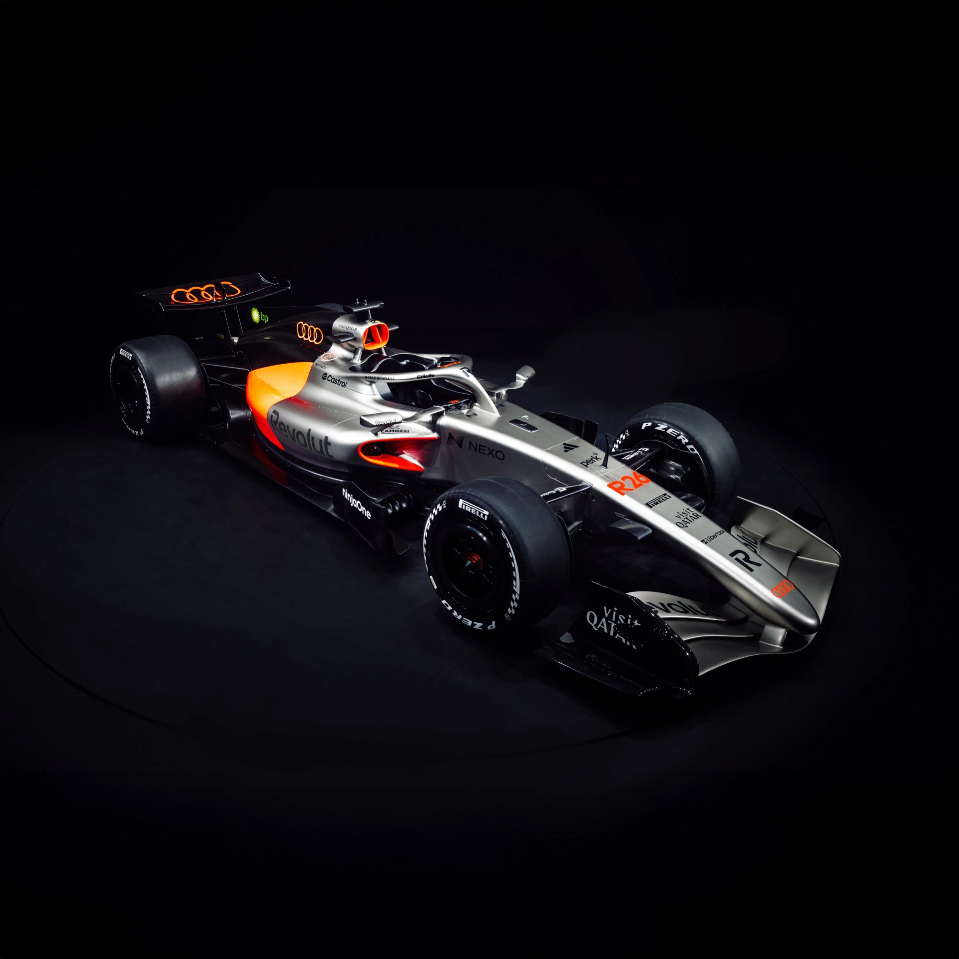 Silver and black Formula 1 race car with orange accents and multiple sponsor logos on a dark background.