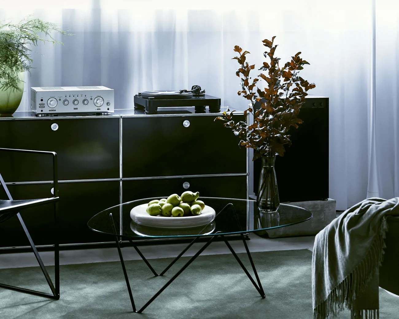 Glass coffee table with black metal legs holding a white plate of green apples in a modern living room.