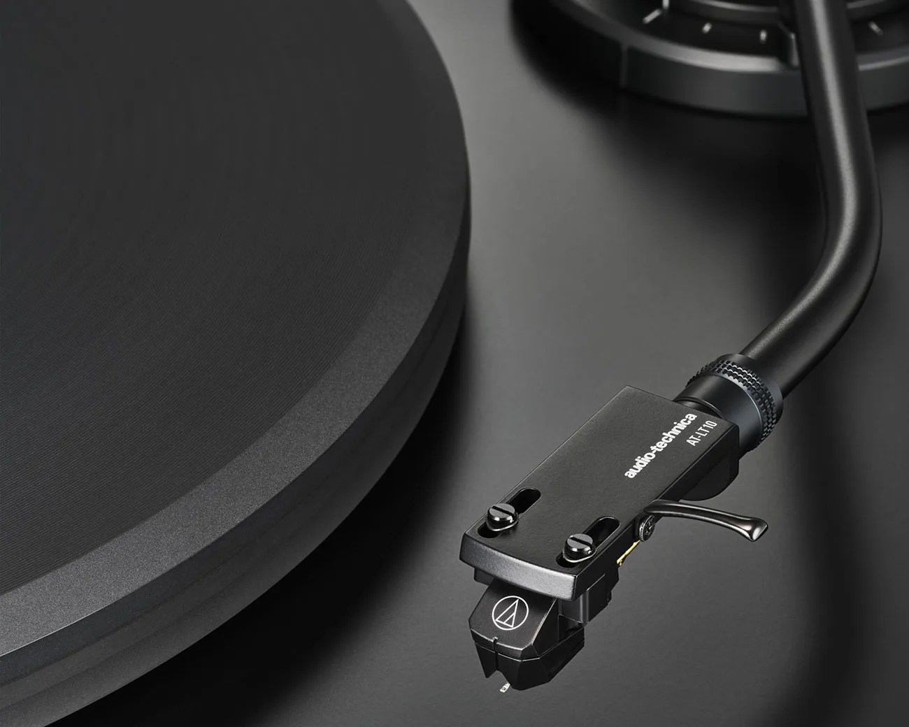 Close-up of a black Audio-Technica AT-LT10 tonearm and cartridge on a matte black turntable.
