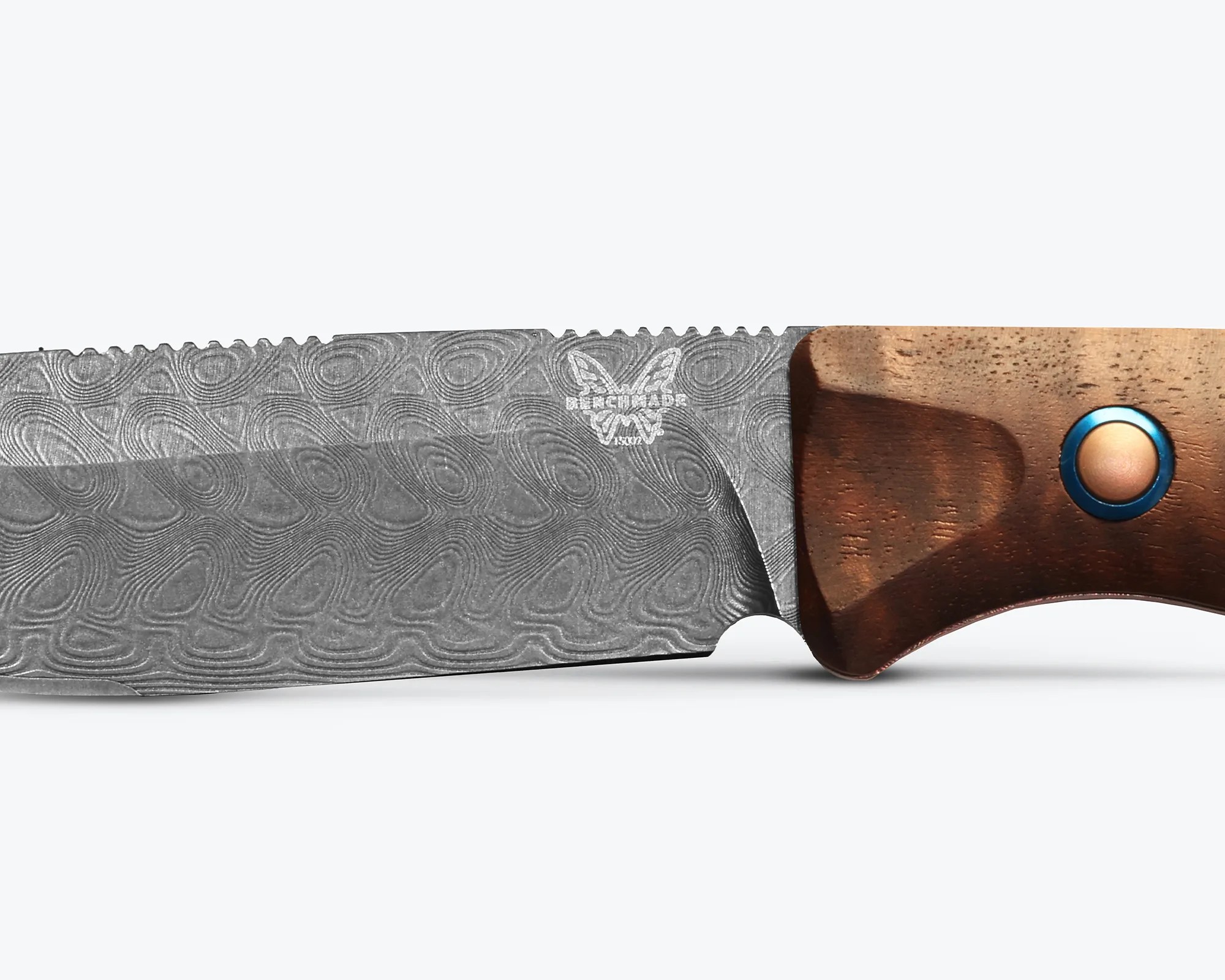 Close-up of a Damascus steel knife blade with a wooden handle featuring a blue circular accent.