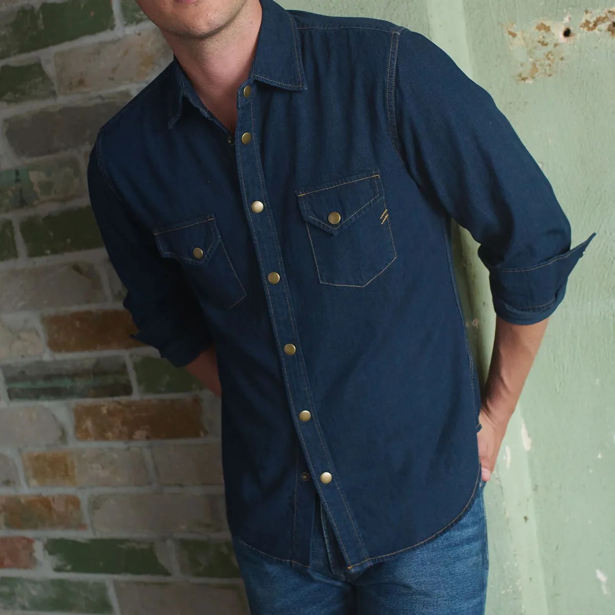 Dark blue denim shirt with rolled-up sleeves and brass snap buttons worn by a person.