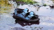 Pair of blue and black sandals with buckles resting on shallow water with grass reflections.