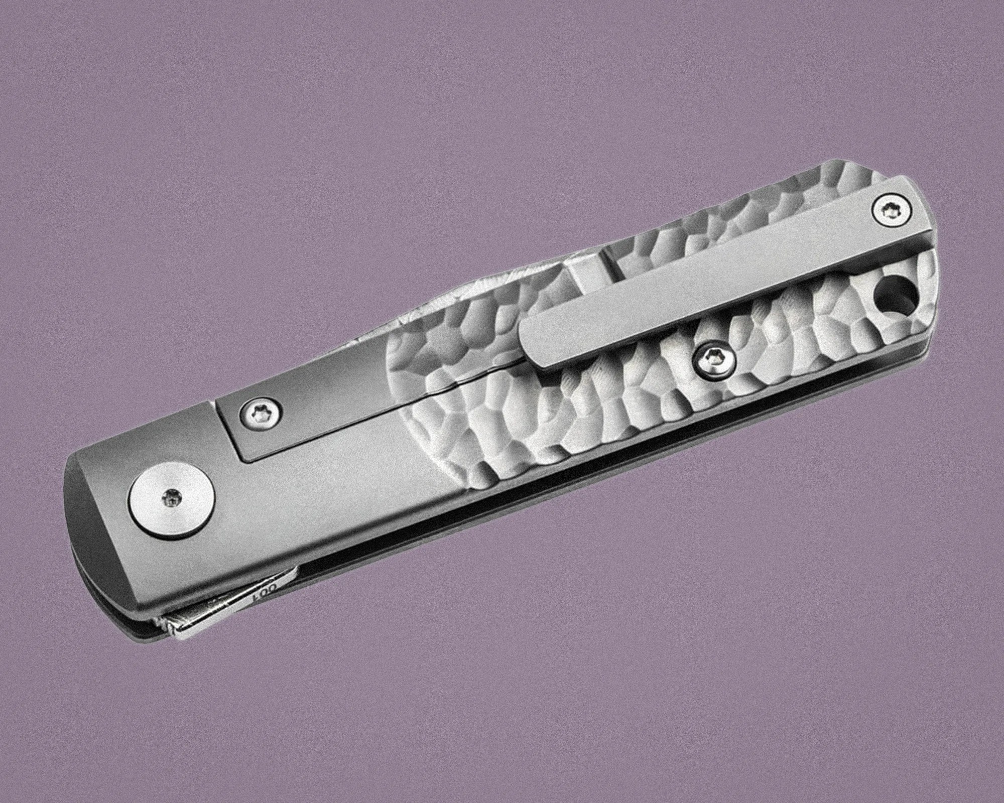 Closed silver folding pocket knife with a textured handle and a clip on a purple background.