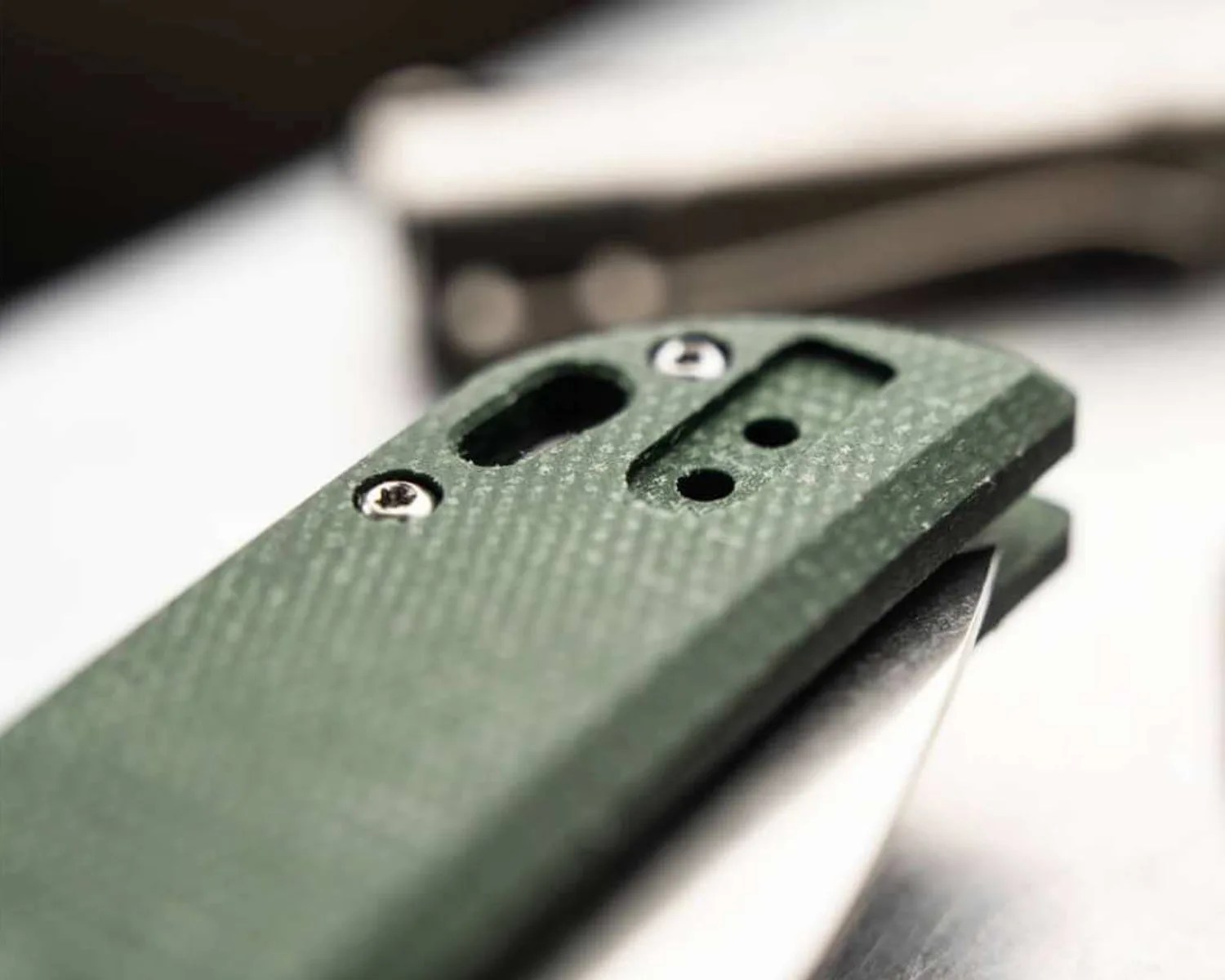 Close-up of a green textured folding knife handle with visible screws and part of the blade.