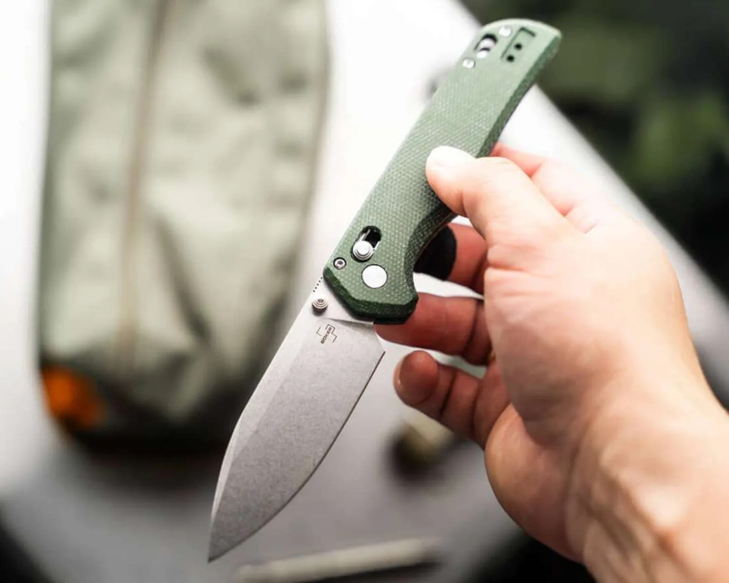 Hand holding a folding knife with a green textured handle and a stonewashed blade.