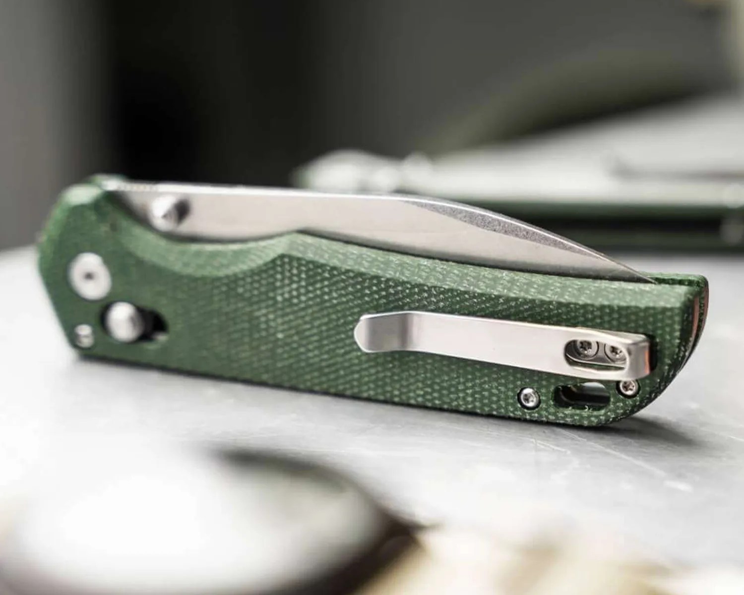 Green textured folding pocket knife with a silver clip on a gray surface.