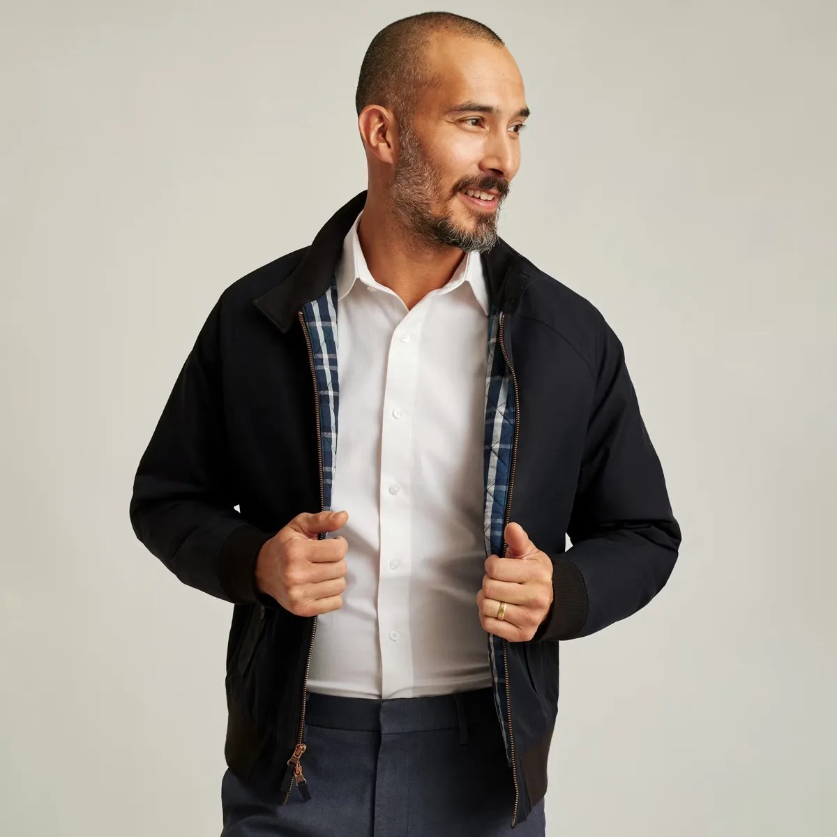 Man wearing a black zip-up jacket with blue plaid lining over a white button-up shirt and dark pants.