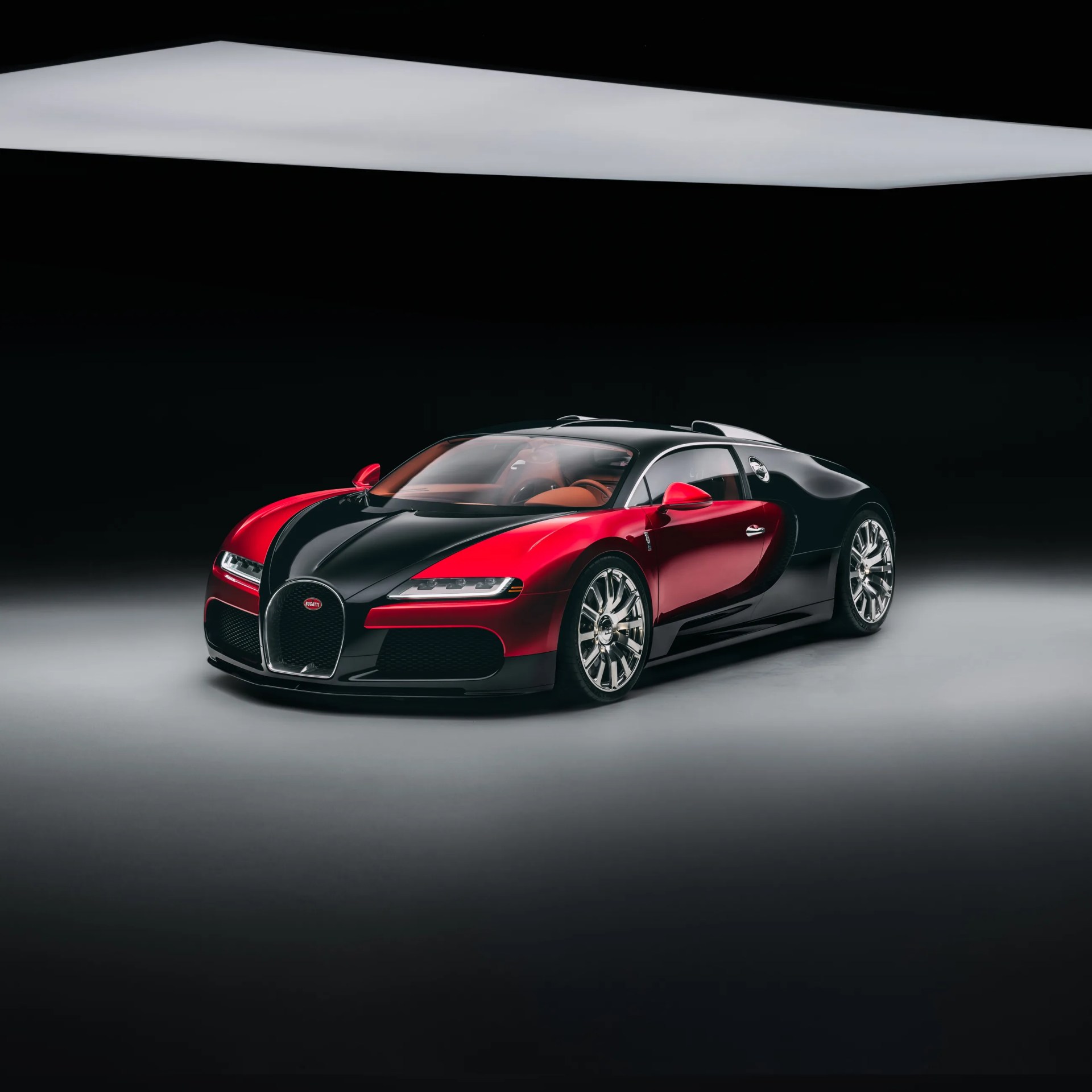 Red and black Bugatti sports car with chrome wheels under studio lighting.