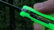 Close-up of a hand holding a folding knife with a bright green handle and partially open blade.