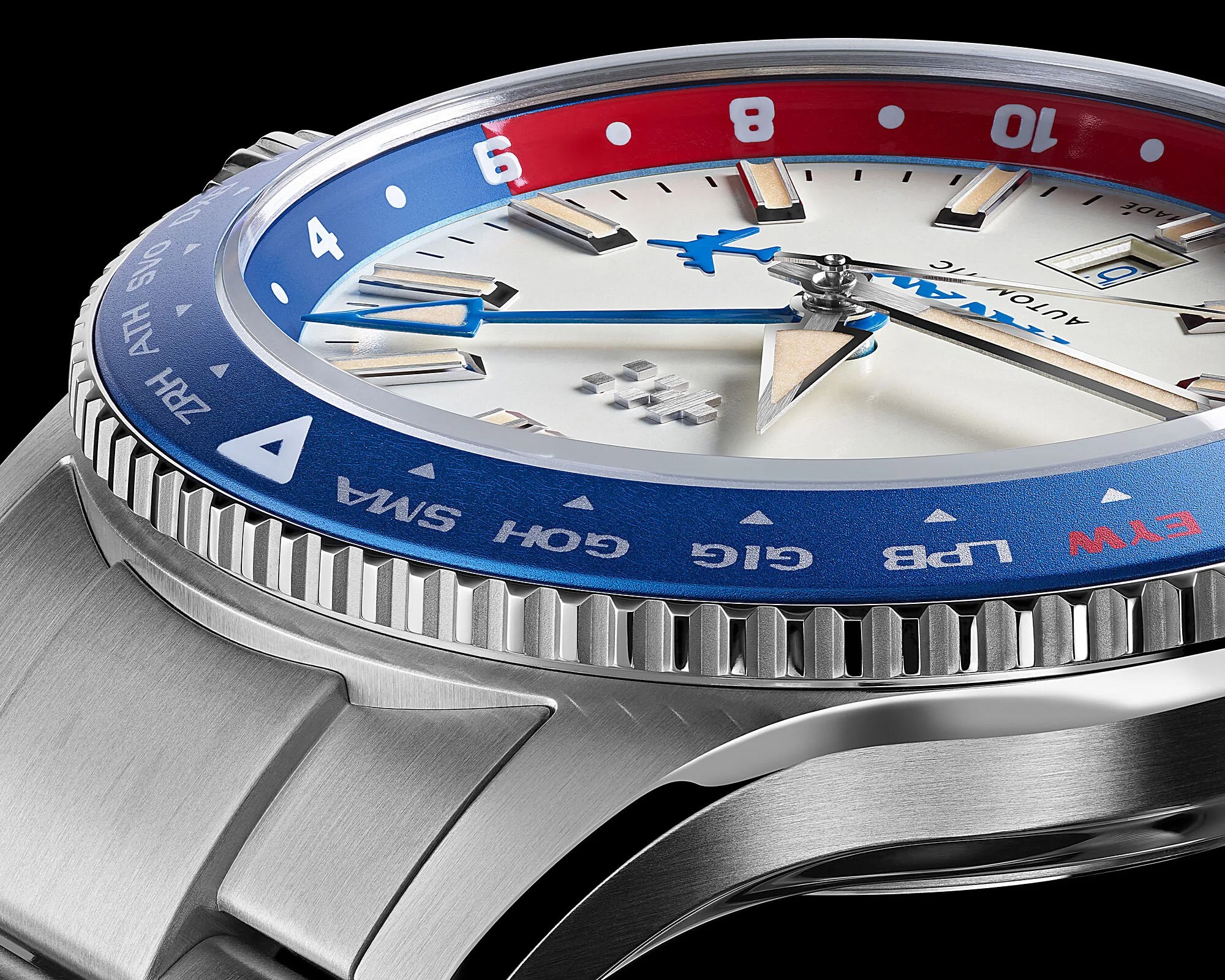 Close-up of a stainless steel wristwatch with a blue and red bezel, white dial, and blue airplane-shaped second hand.