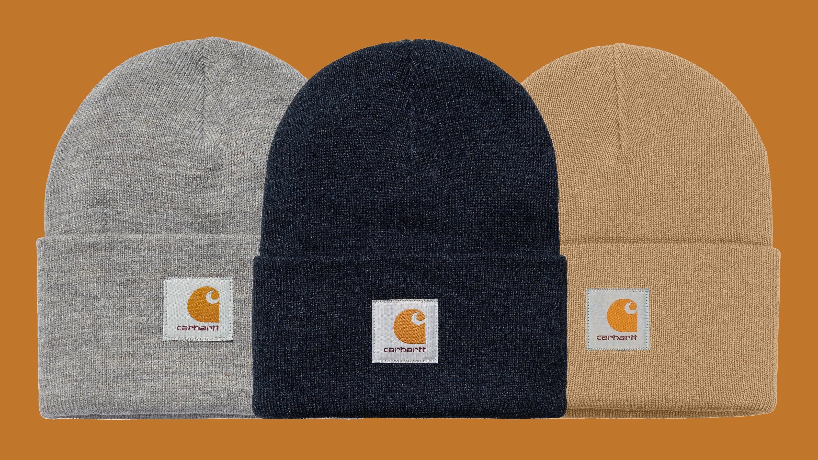 Three Carhartt knit beanies in gray, black, and tan with folded cuffs and logo patches on a brown background.