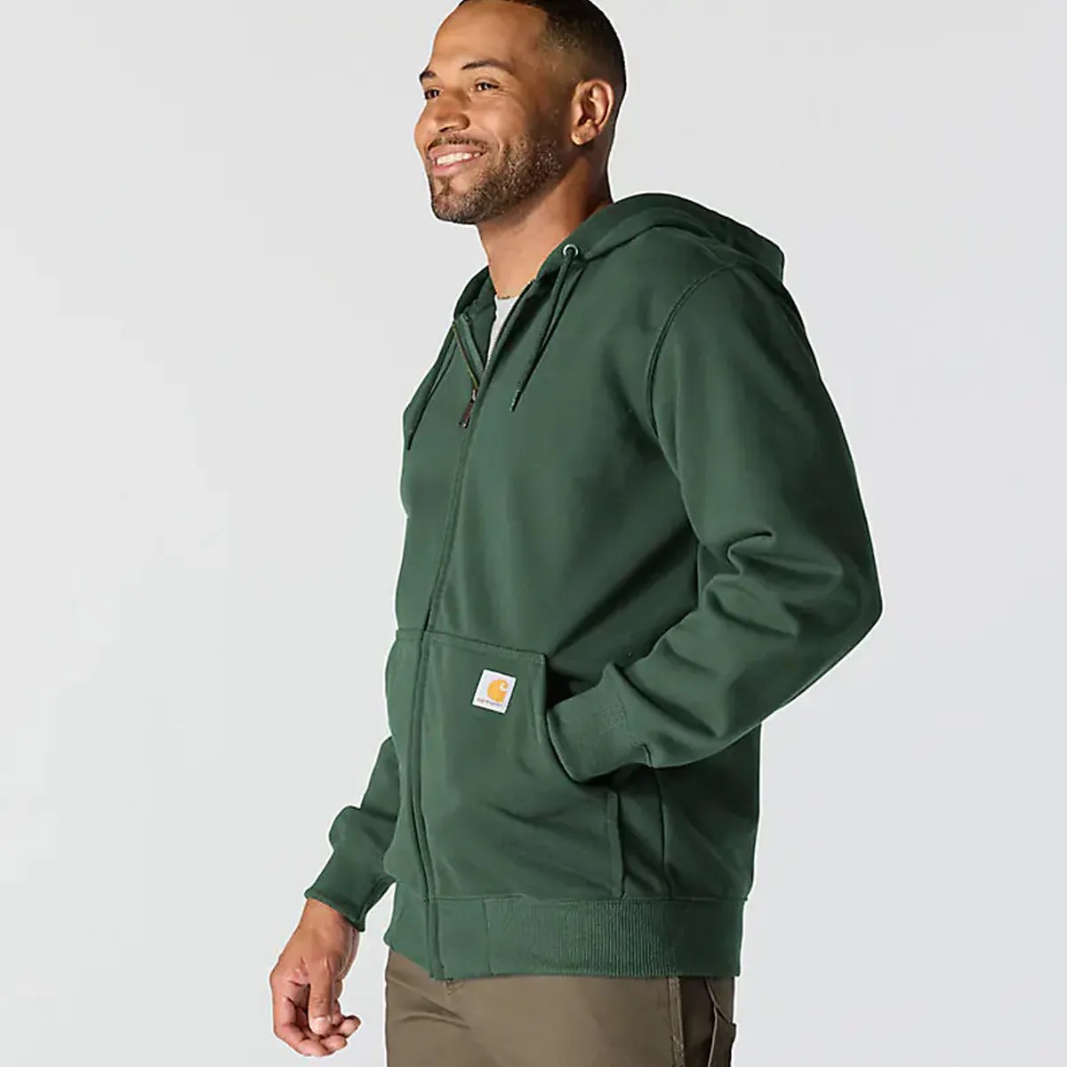 Dark green zip-up hoodie with front pockets and a small logo patch on the pocket, worn by a person.