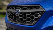 Close-up of a blue car's front grille with a Subaru logo and water droplets on the surface.