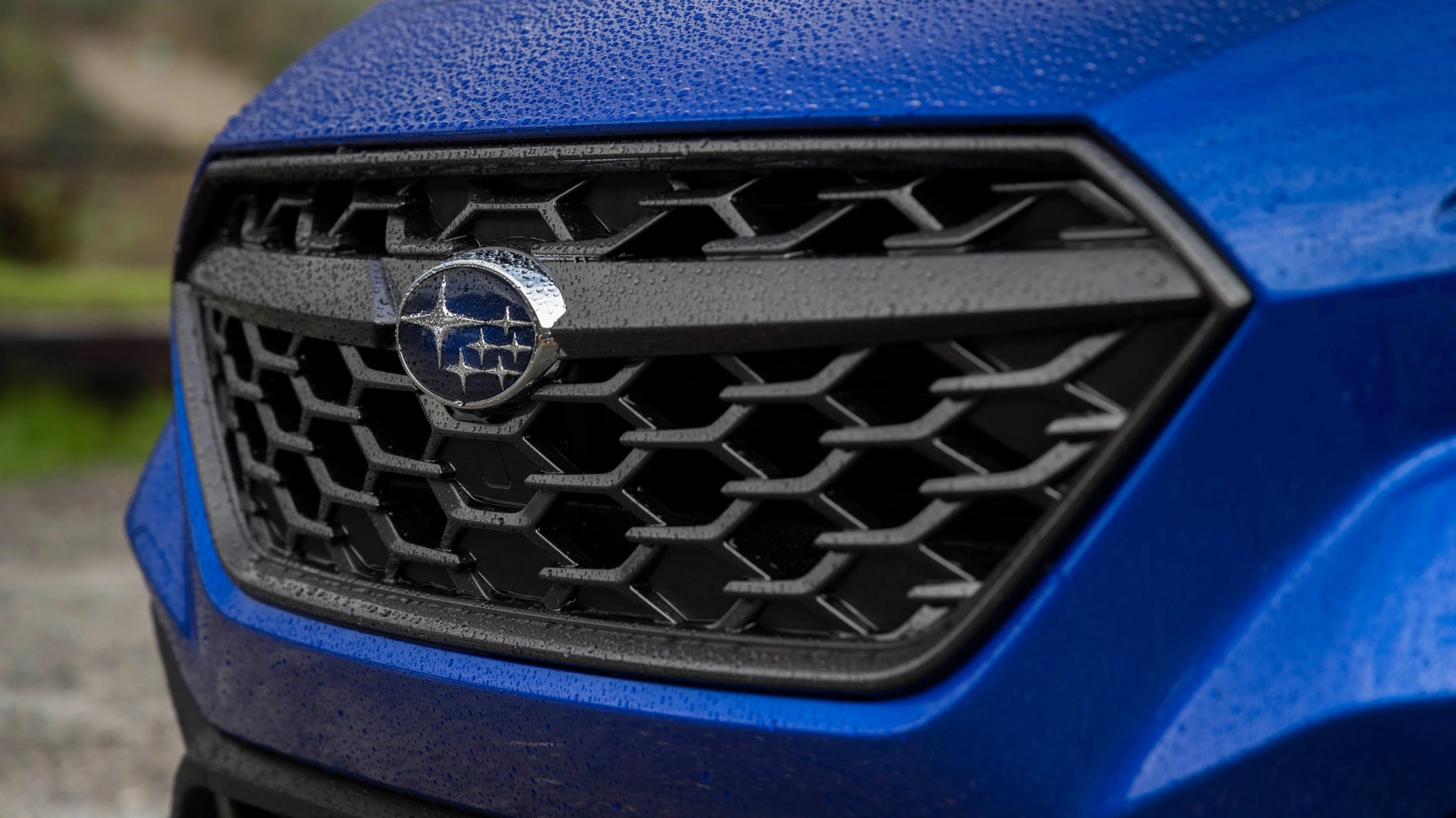 Close-up of a blue car's front grille with a Subaru logo and water droplets on the surface.