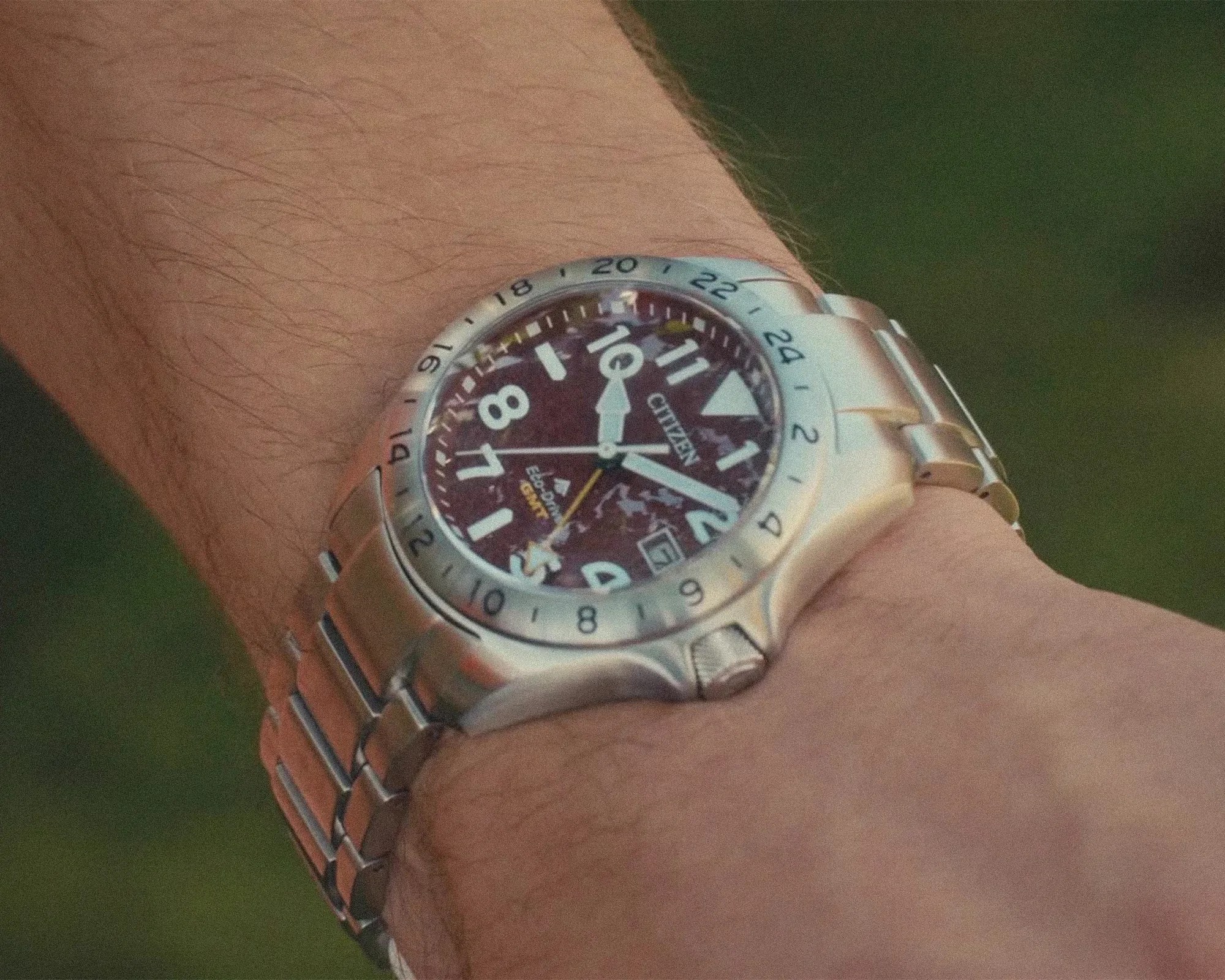 Silver Citizen Eco-Drive GMT wristwatch with a maroon dial and metal link band on a wrist.