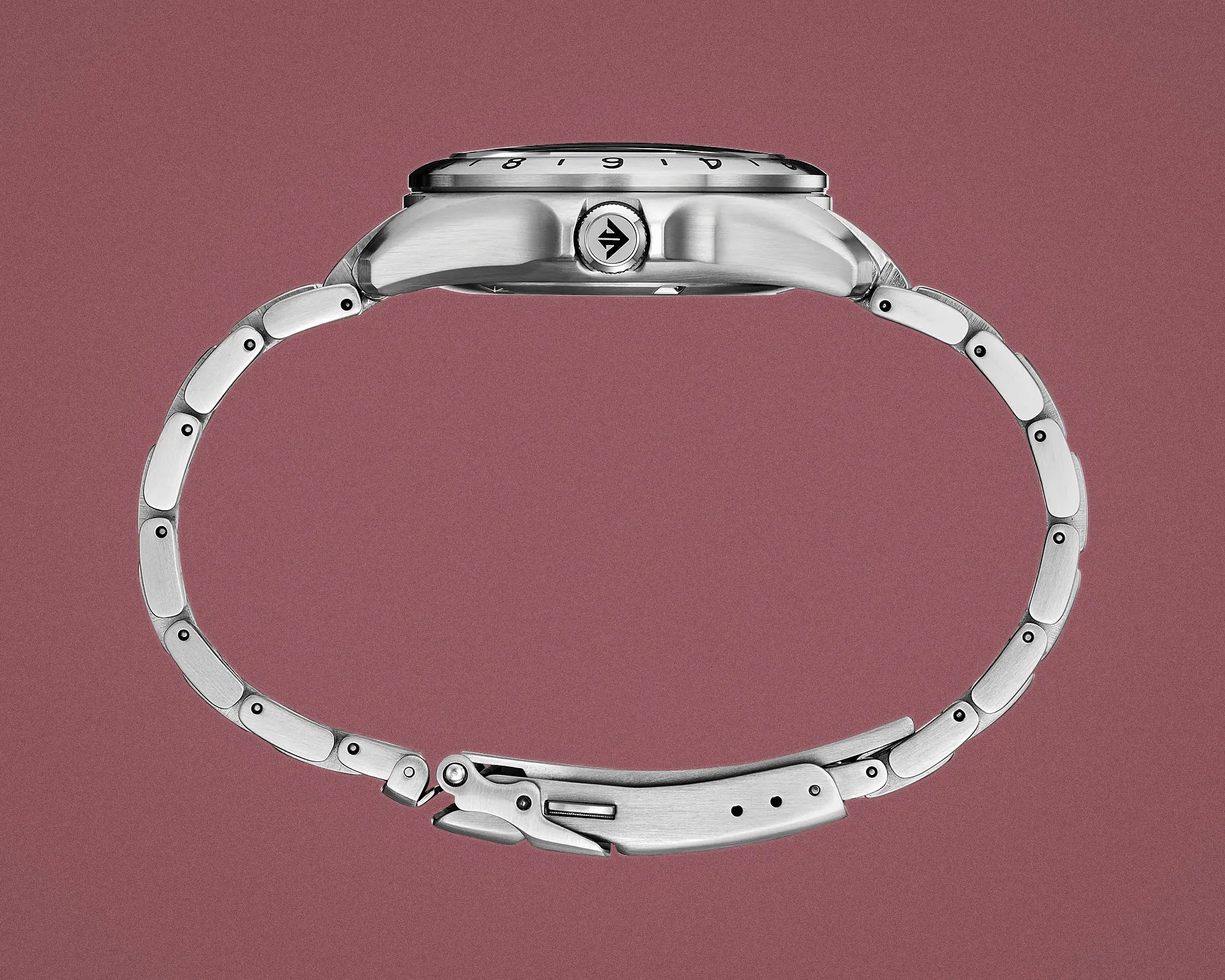 Side view of a silver metal wristwatch with a linked bracelet and a crown on a mauve background.
