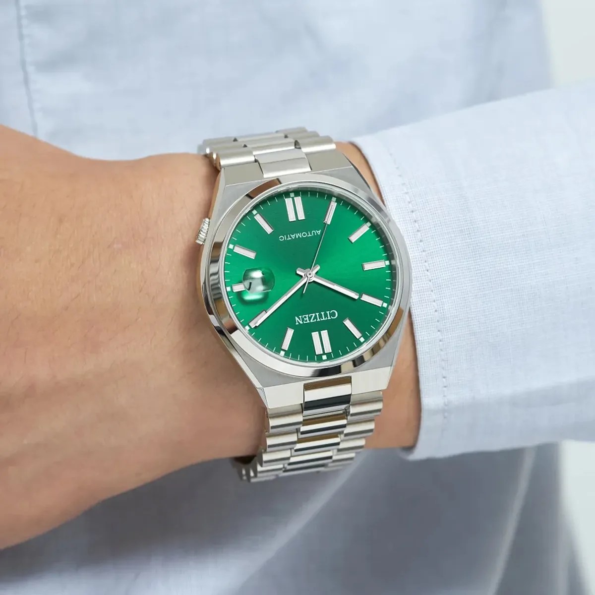Silver metal Citizen wristwatch with a green dial and date magnifier worn on a wrist.