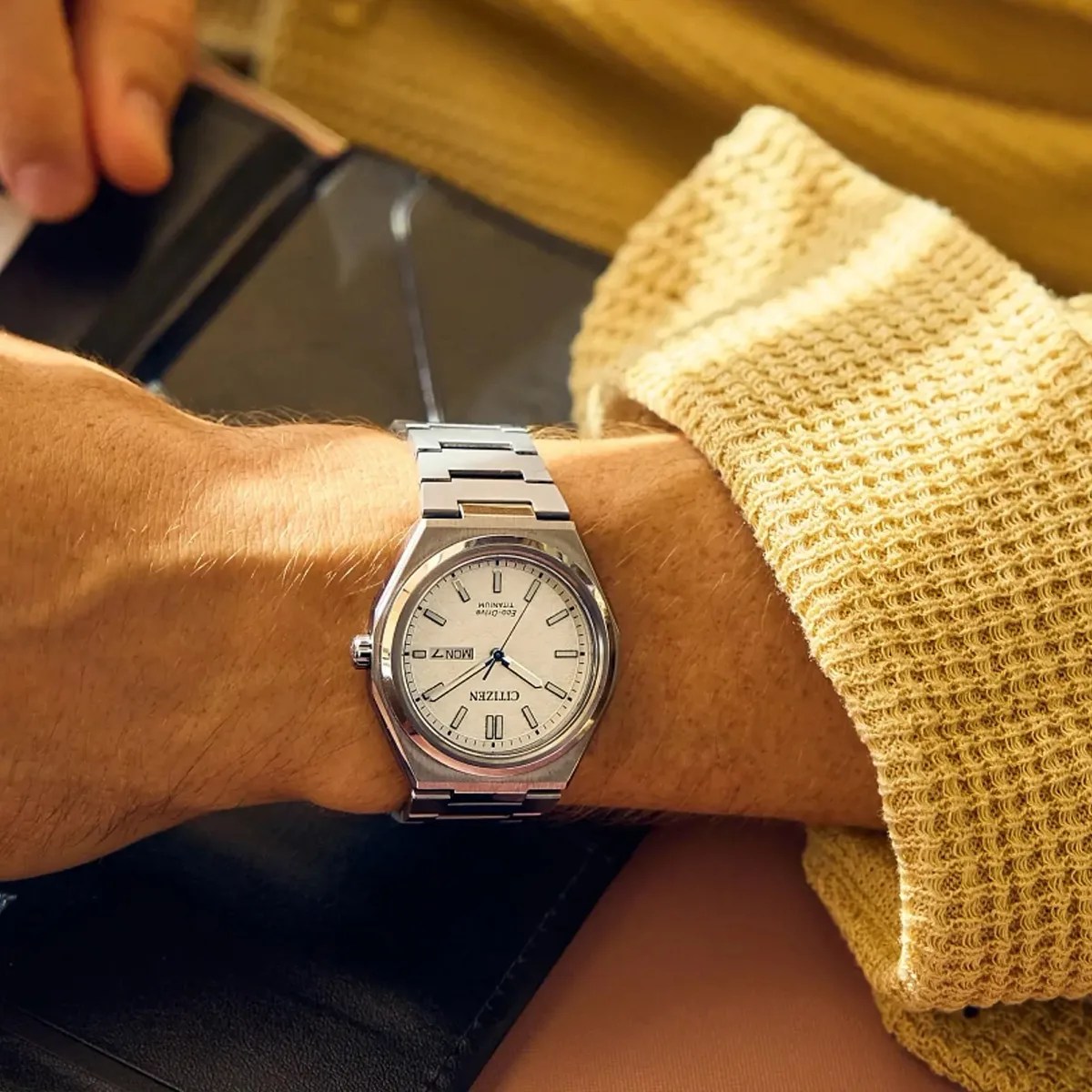 Silver Citizen Eco-Drive Titanium wristwatch with white dial and day-date display worn on a wrist.