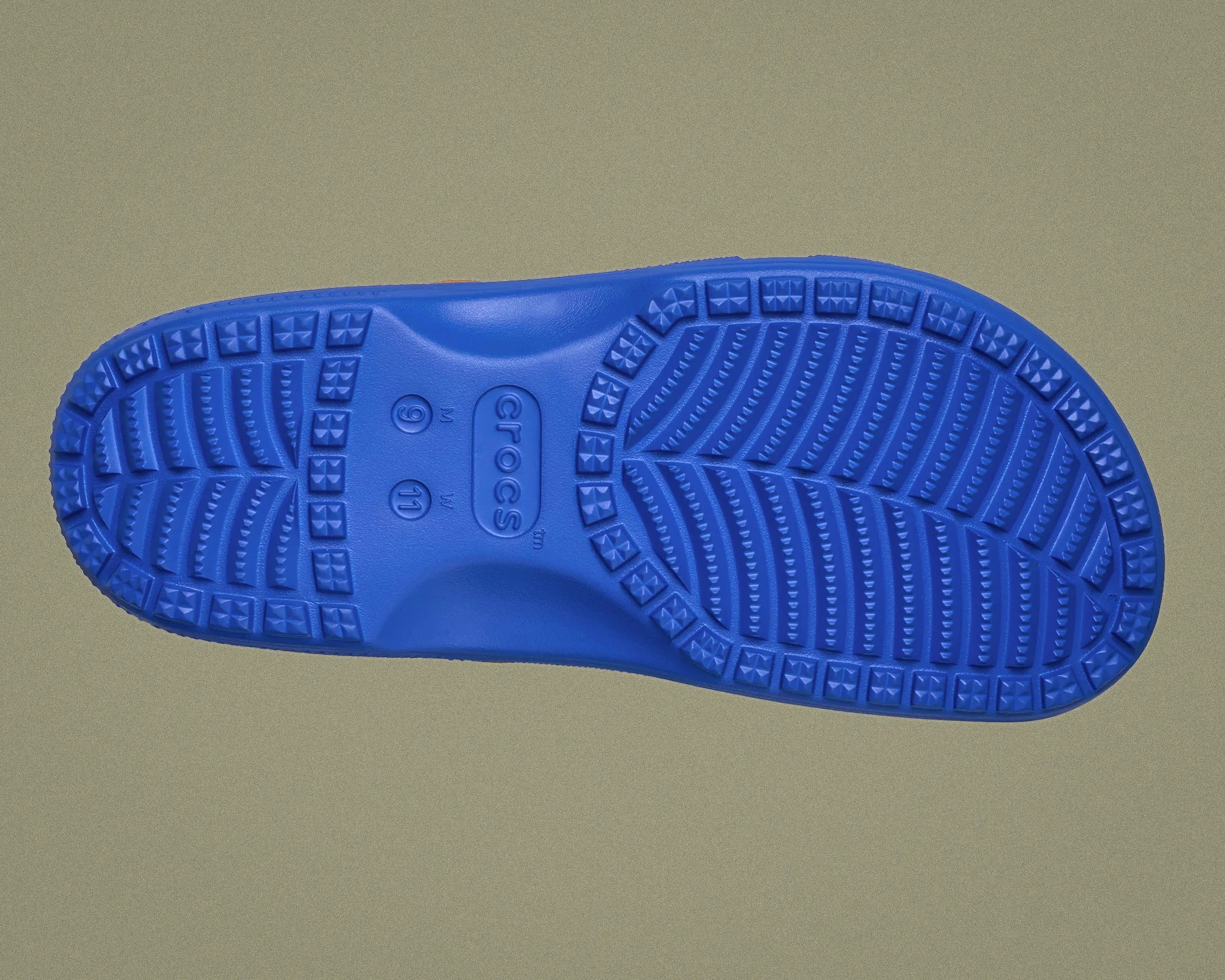 Blue Crocs shoe sole with textured tread pattern and size markings on a gray background.