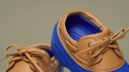Pair of blue rubber shoes with tan leather trim and laces on a neutral background.