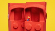 Pair of red LEGO-themed Crocs with a small LEGO minifigure standing between them against a yellow background.