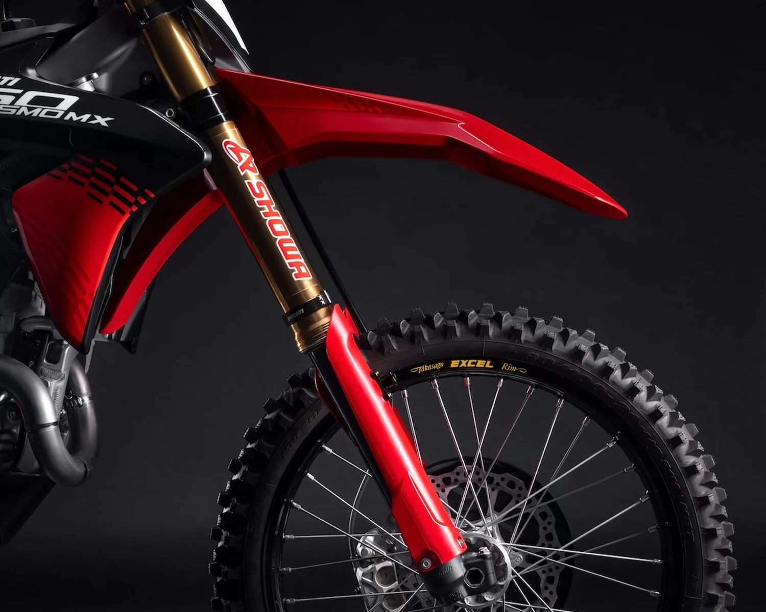 Front wheel and suspension fork of a red and black dirt bike with Showa branding on the gold fork tube.