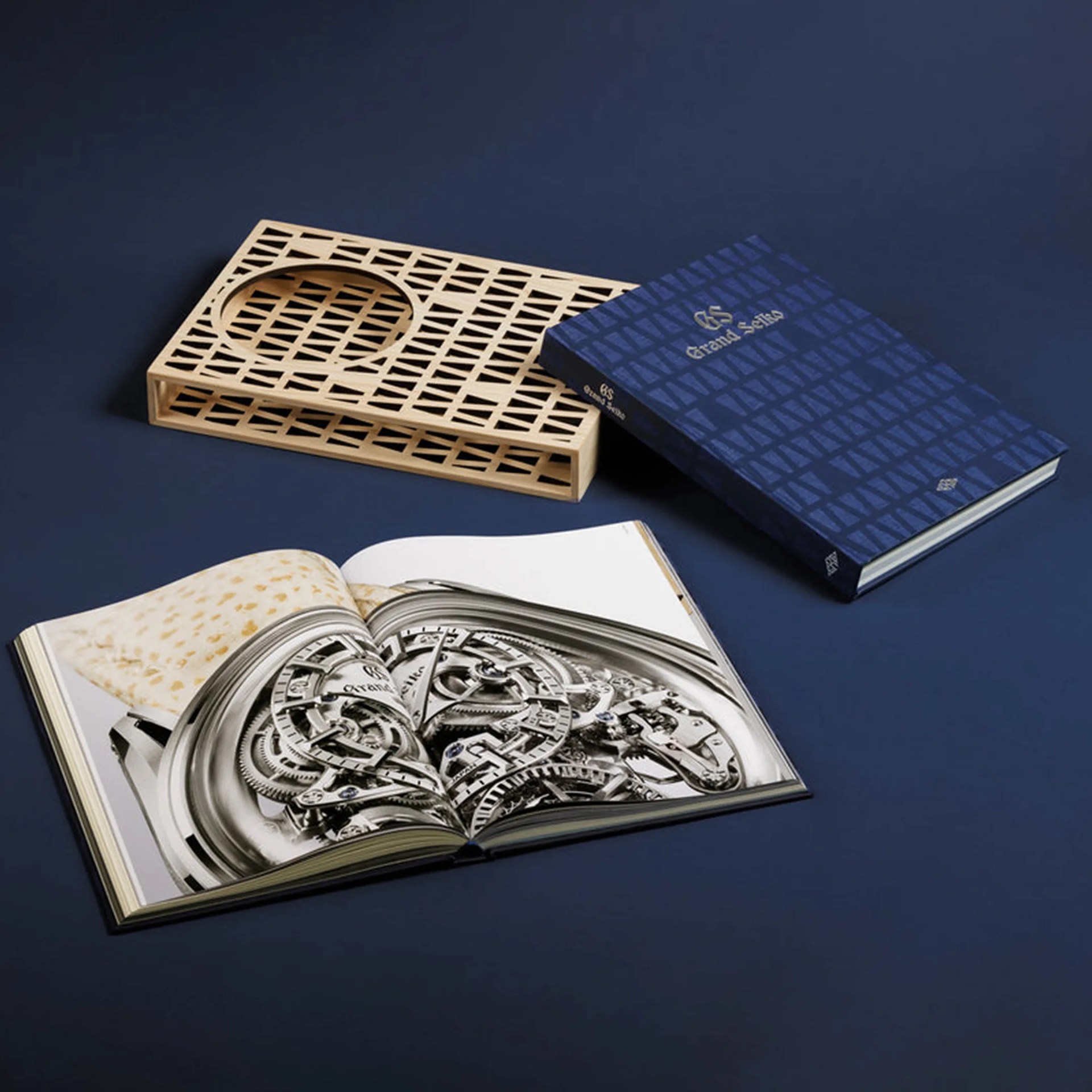 Blue hardcover book titled "Grand Seiko" with a wooden lattice book holder and an open book showing a detailed watch mechanism.