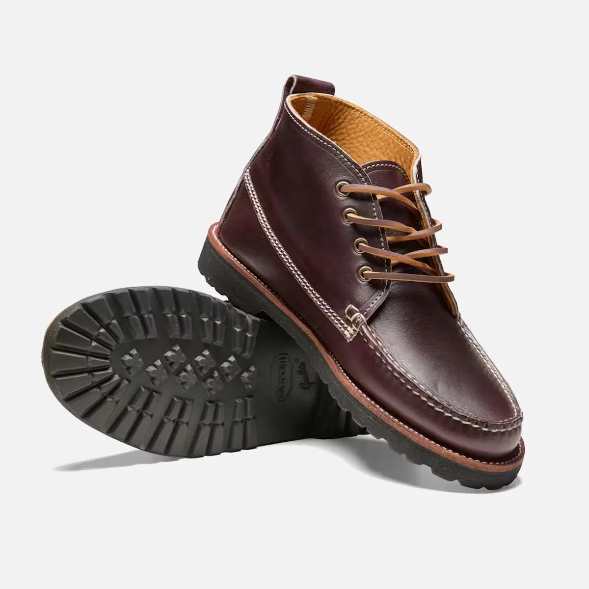 Pair of dark brown leather moc toe boots with tan laces and black lug soles on a white background.