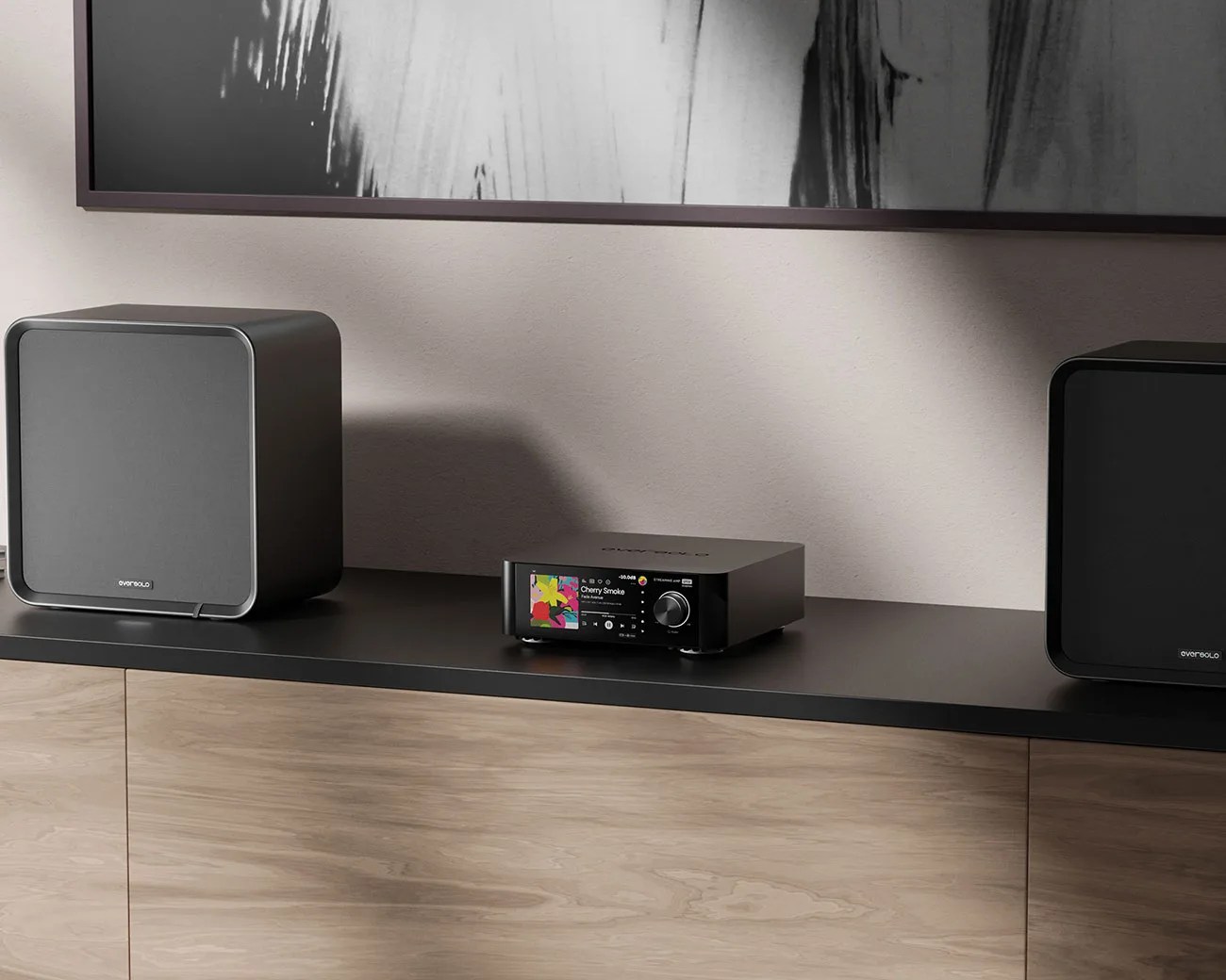 Black compact stereo receiver with digital display and volume knob between two black EverSolo speakers on a black shelf.