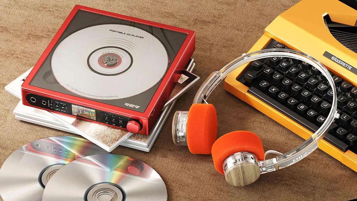 Red portable CD player with a clear top, orange foam headphones, and a yellow Silverette typewriter on a brown surface.