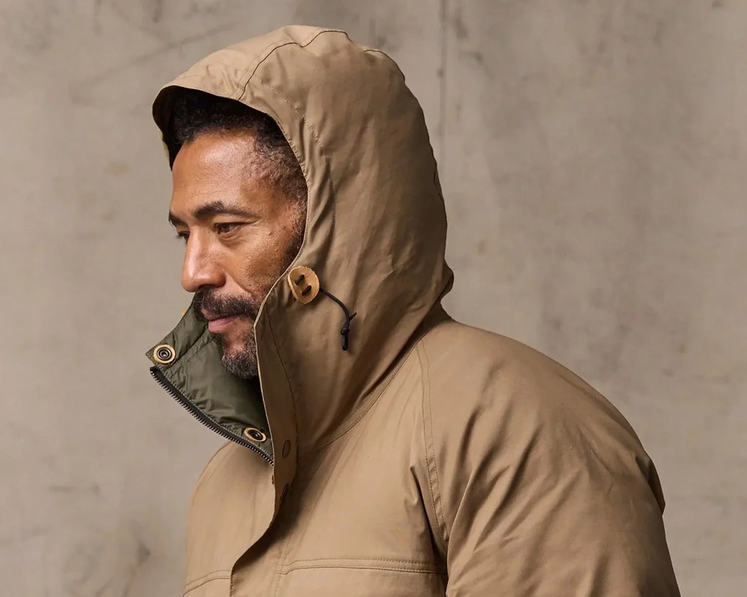 Man wearing a tan hooded jacket with wooden toggle buttons and a green inner lining.