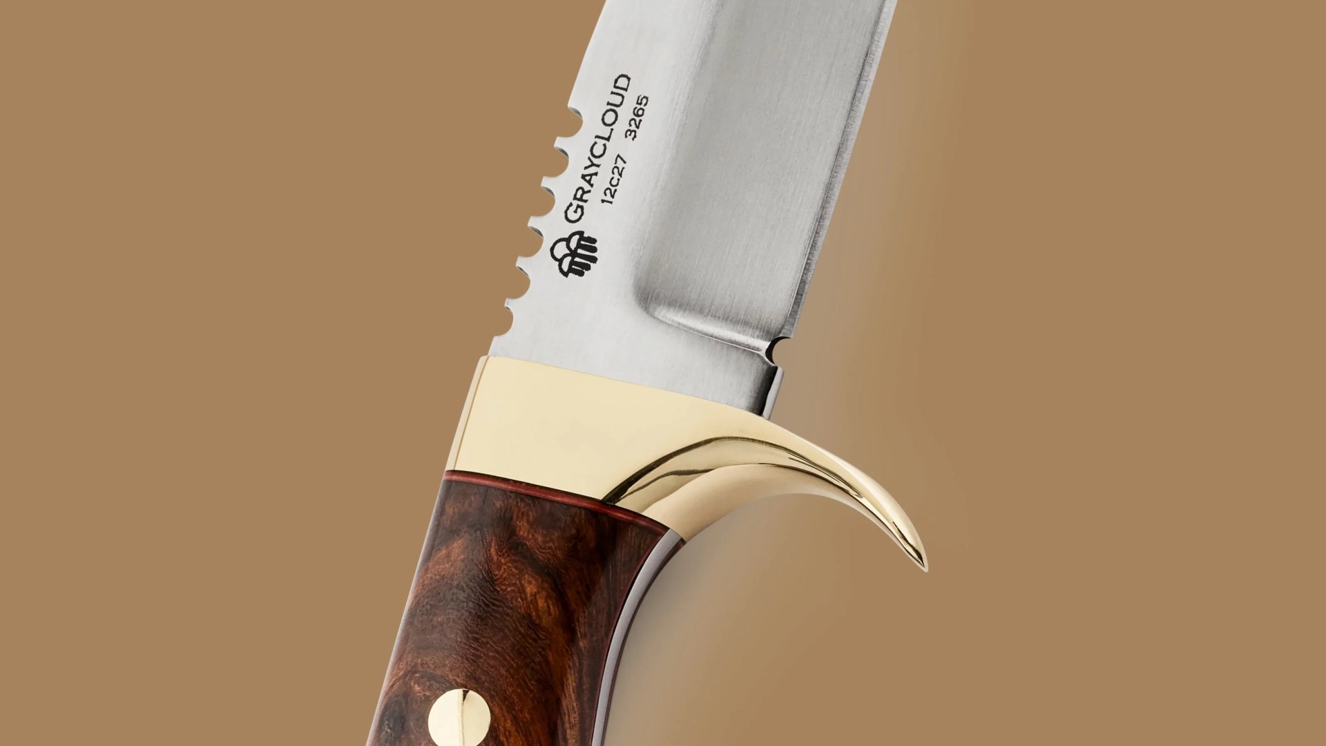 Close-up of a Graycloud serrated knife blade with a polished brass guard and dark wood handle.