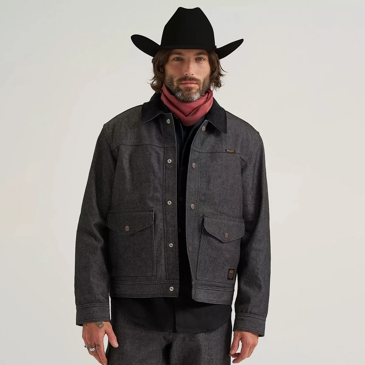 Man wearing a dark gray denim jacket with flap pockets and a black collar, paired with a black cowboy hat and red neckerchief.
