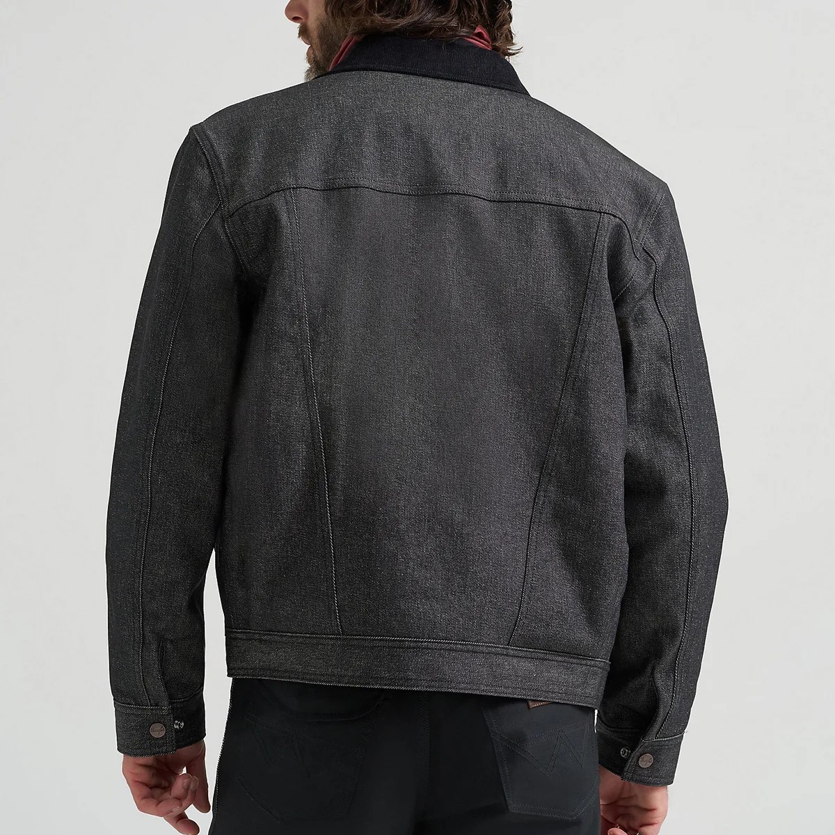 Back view of a person wearing a dark gray denim jacket with buttoned cuffs and visible seam detailing.